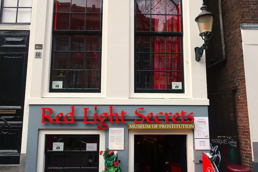 Entrance to Red Light Secrets, the Museum of Prostitution located on Oudezijds Achterburgwal in Amsterdam’s Red Light District, housed in a traditional canal building with red curtains.