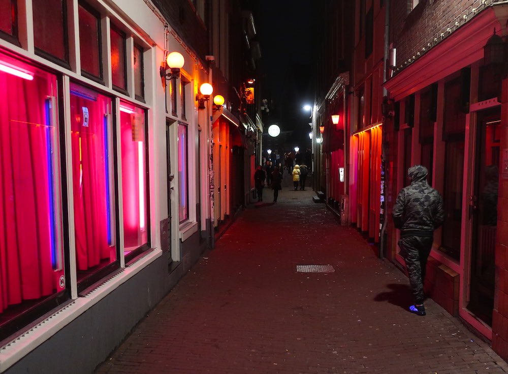 man walking in one of the alleys in Amsterdam Red Light District surrounded by red-lit windows at night
