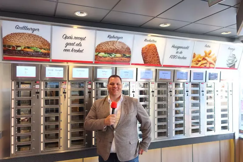 Dennis de Borst, CEO of FEBO, standing inside the FEBO location on Oudezijds Voorburgwal in Amsterdam’s Red Light District, in front of the iconic vending wall selling kroket and other Dutch snacks.