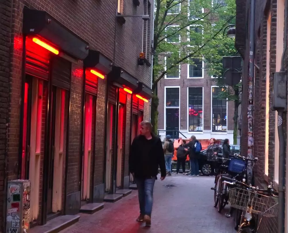 a man walks past red-lit window brothels in De Wallen, Amsterdam's Red Light District