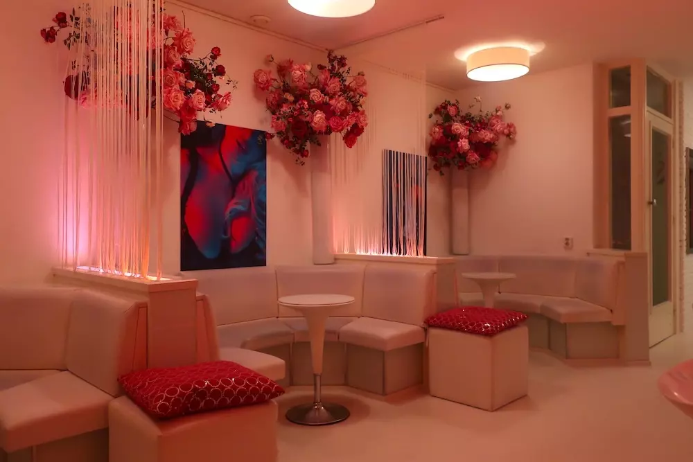 the white and modern interior of Amsterdam brothel Club LV with tables, sofas and flowers on the wall