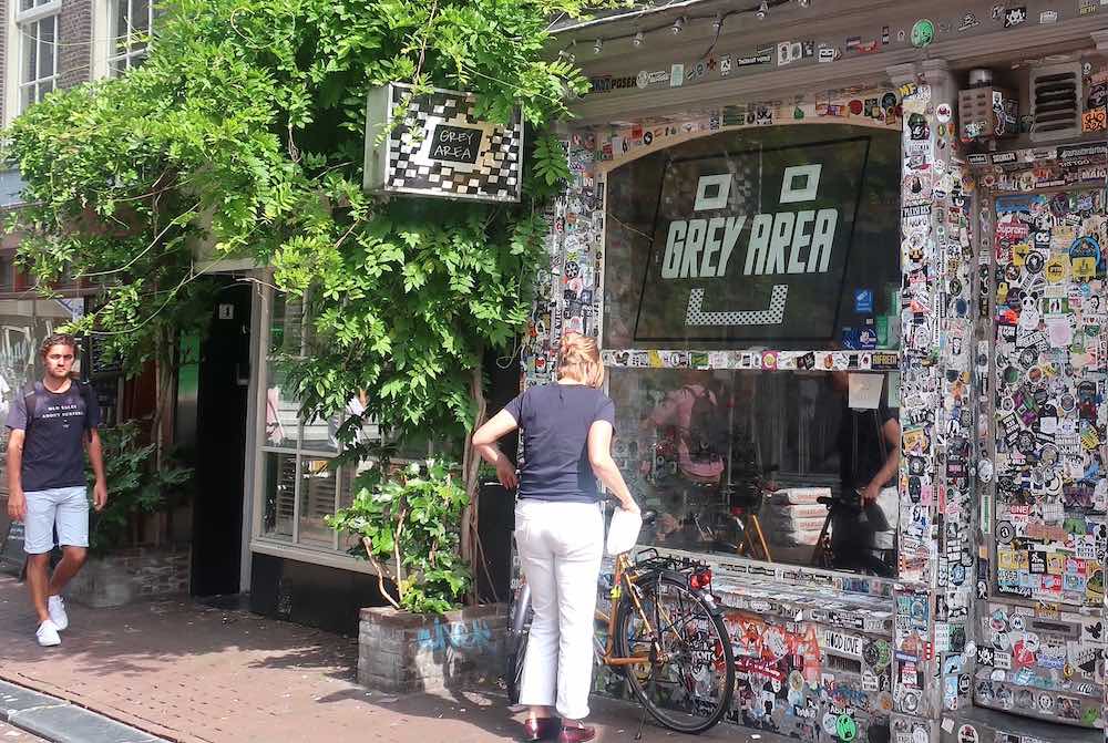 the front of coffee shop grey area in Amsterdam with a woman in front parking her bicycle