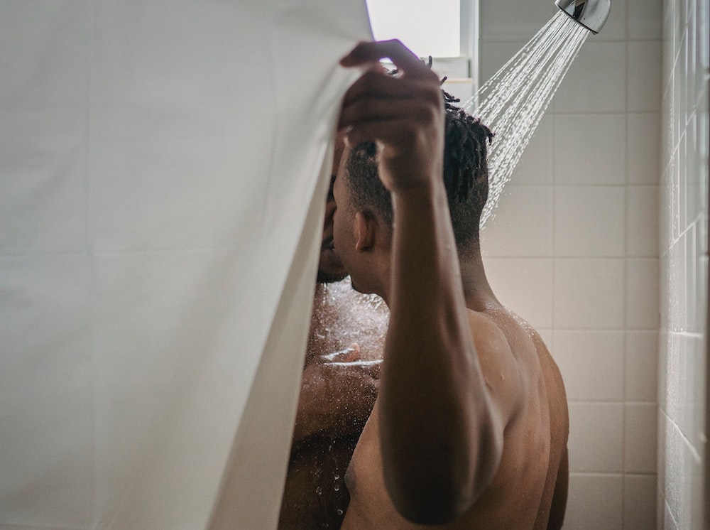 Two gay men kissing in the shower while closing the shower curtain