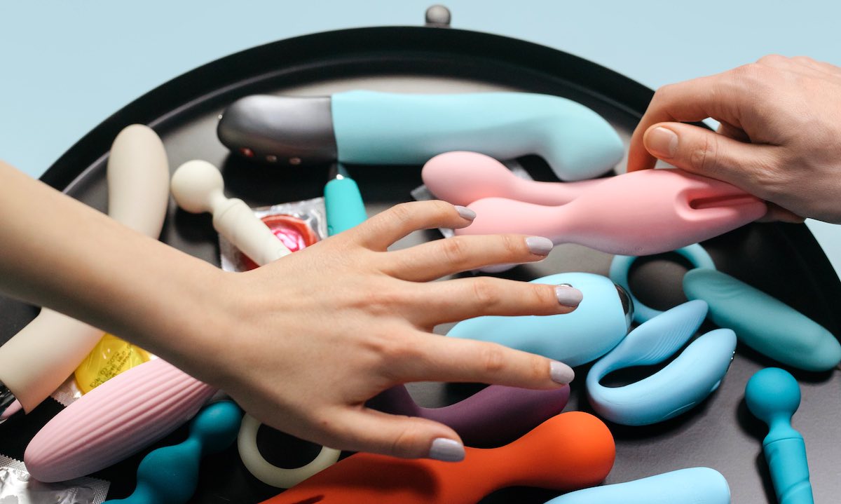 two white hands picking coloured sex toys on a black table
