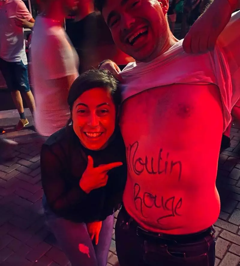 Eine Frau zeigt auf den Bauch eines Mannes ohne T-Shirt, auf dessen Körper im Amsterdamer Rotlichtviertel der Schriftzug „Moulin Rouge“ steht.