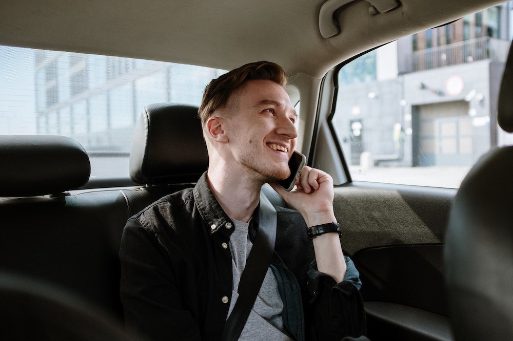 male traveller making a phone call in an Uber cab while looking out of the window and smiling