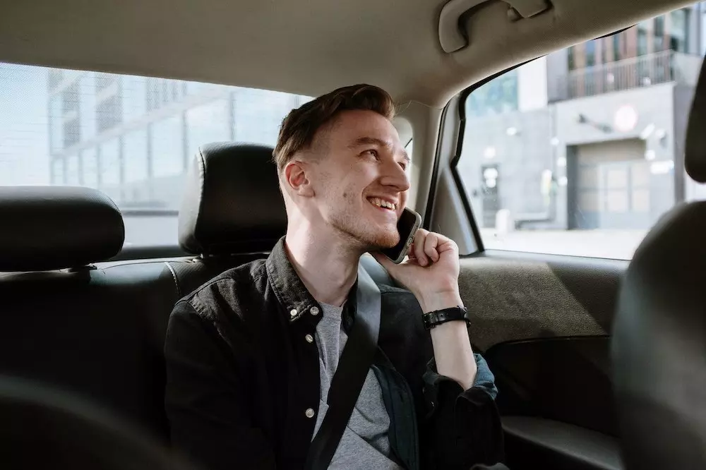 male traveller making a phone call in an Uber cab while looking out of the window and smiling