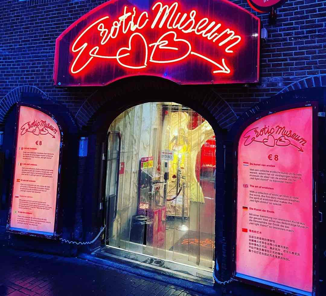 the front of the Erotic Museum in Amsterdam Red Light District at night with red neon letters showing the name of the museum and pink doors.