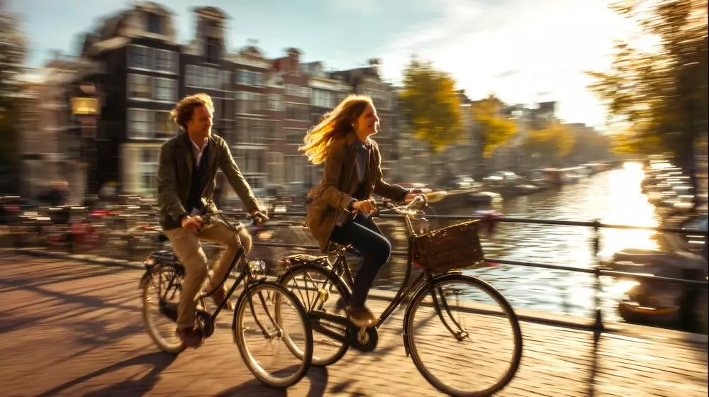 A couple cycling across an Amsterdam canal bridge on a sunny autumn day