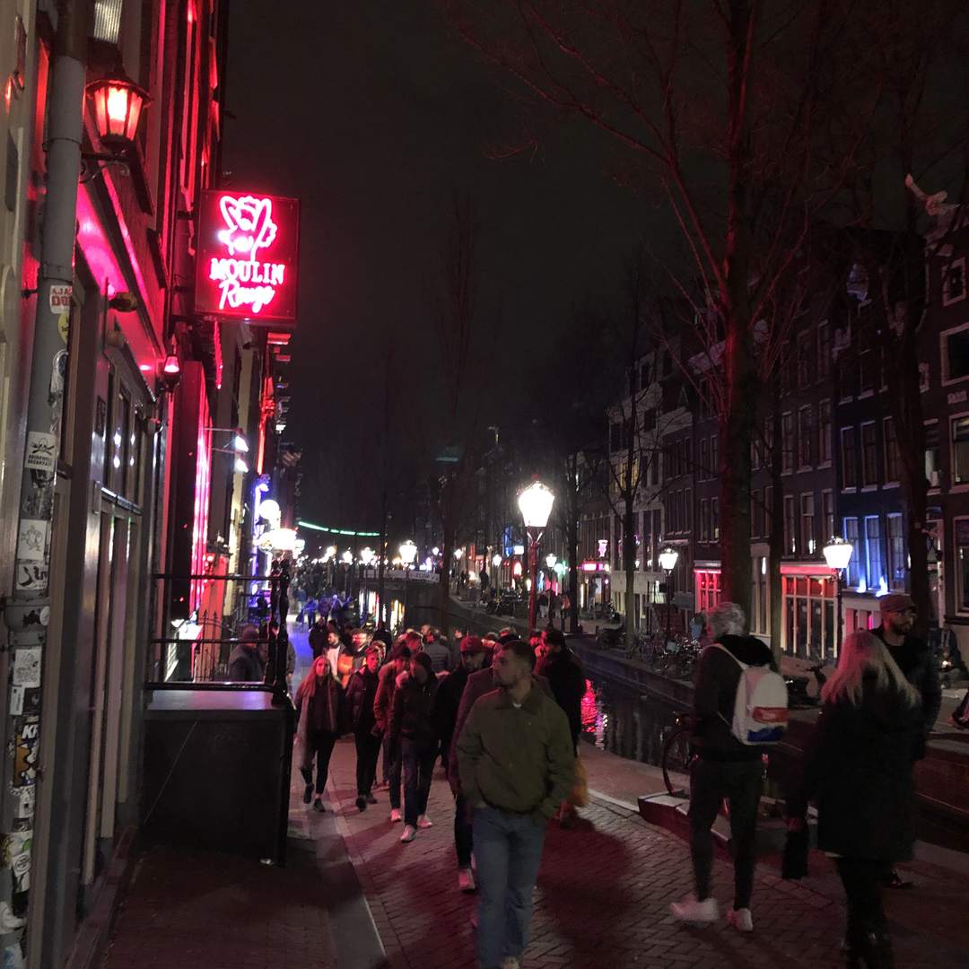 Het Moulin Rouge neonbord aan een drukke Oudezijds Achterburgwal op de Amsterdamse Wallen bij nacht